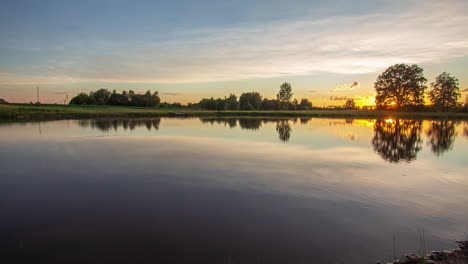 timelapse shot of sun going down in the background over pristine lake along rural countryside during evening time