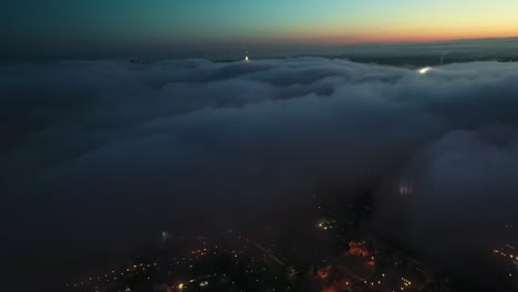 aerial birds eye shot over dark cloudscape and illuminated city on the valley at sunrise time