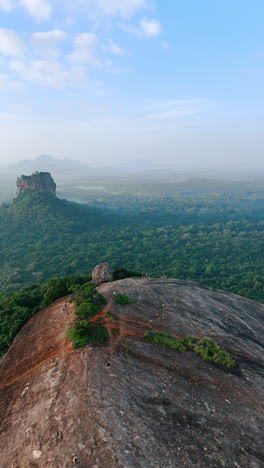 flying over the high mountain with rounded bare top. some people walk by the rock. sri lanka aerial view. vertical video.