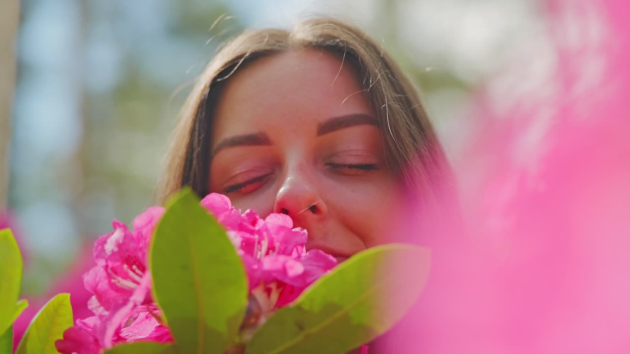 Ritratto al rallentatore di una donna che si gode il profumo del rododendro sotto la calda luce del sole.