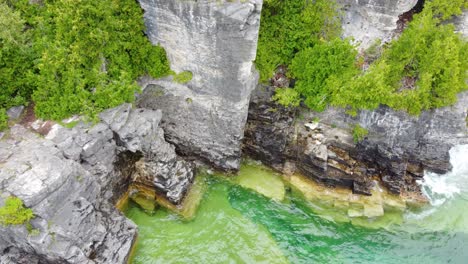 aerial top down view of the ocean waves washing up against a rocky cliff along the coastline of georgian bay, ontario, canada