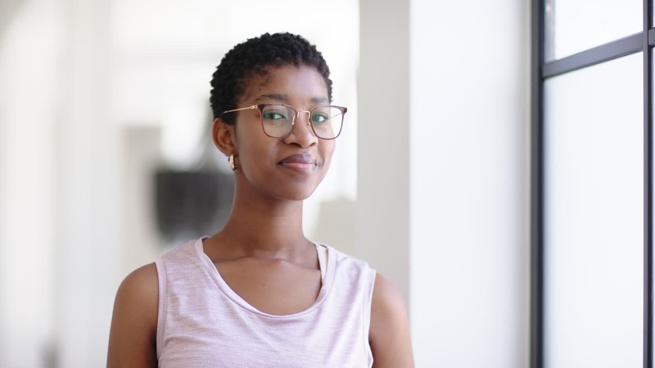 African American woman standing near large window, turning toward camera noticing lens and smiling