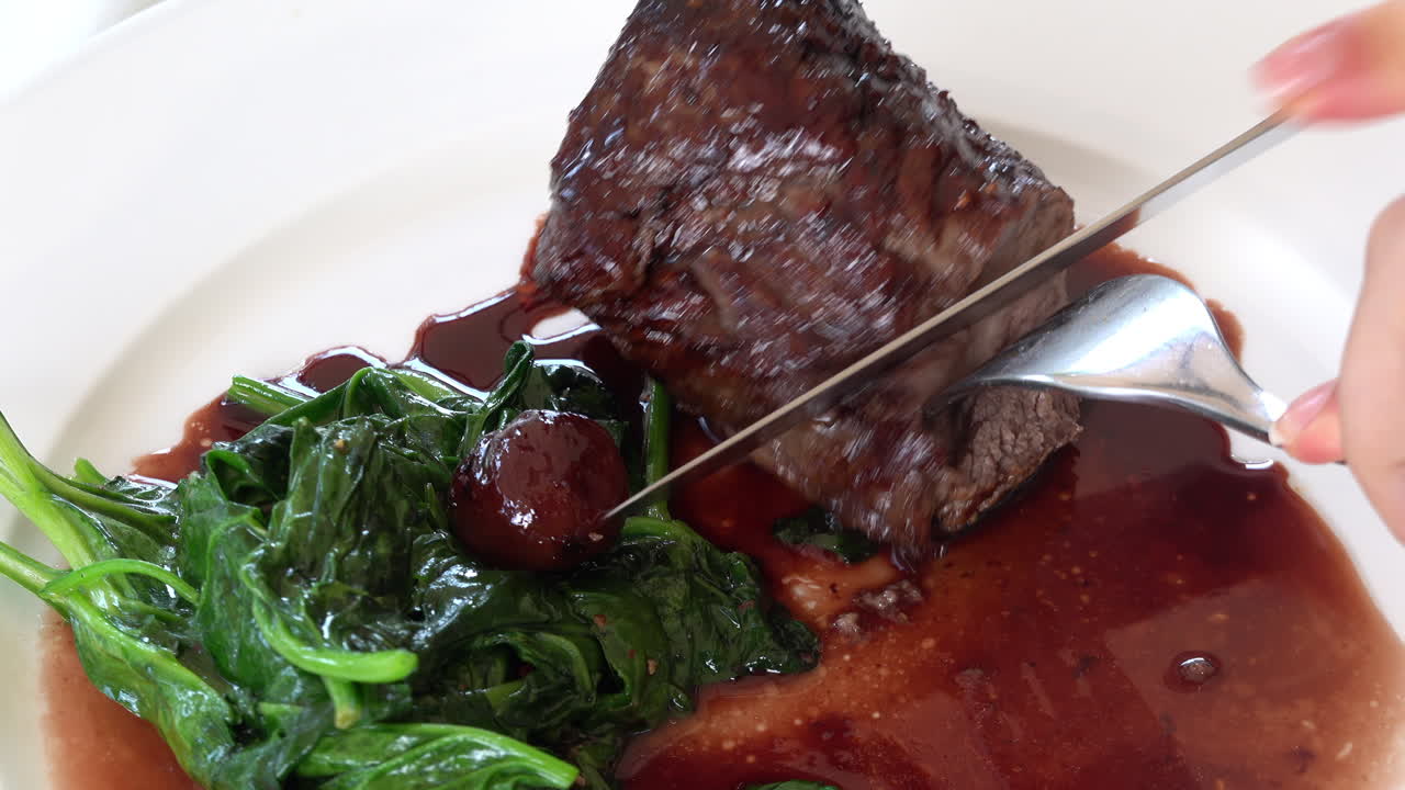 Woman cutting up a cooked beef tenderloin in sauce with greenery on a white plate