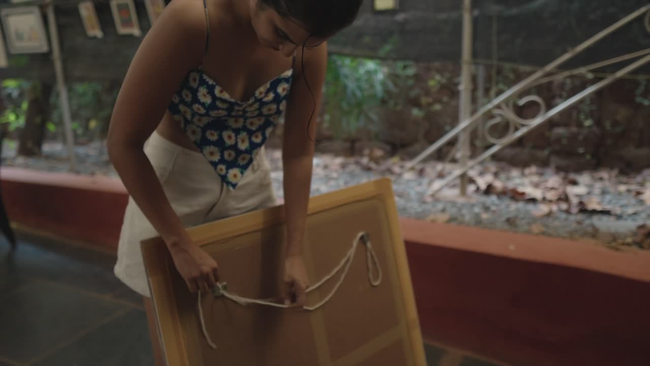 In a mesmerizing slow-motion detail clip of a young woman's meticulous hands prepare a picture rope with grace and precision, enhancing an art gallery's ambiance