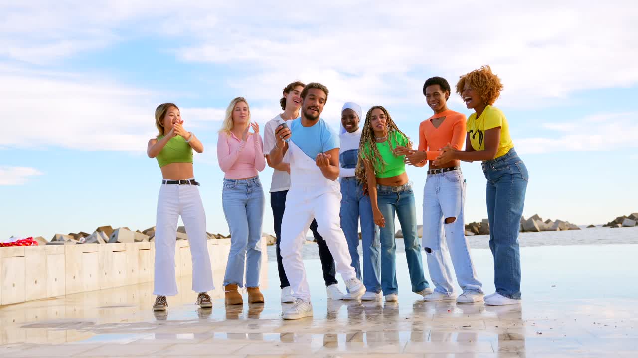 Gruppo di giovani adulti diversi che ballano e cantano sulla spiaggia