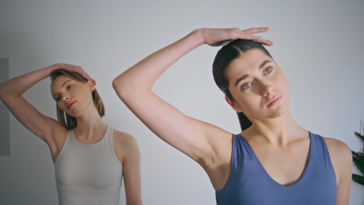 Athletes couple stretching neck practicing yoga indoors. Women training together