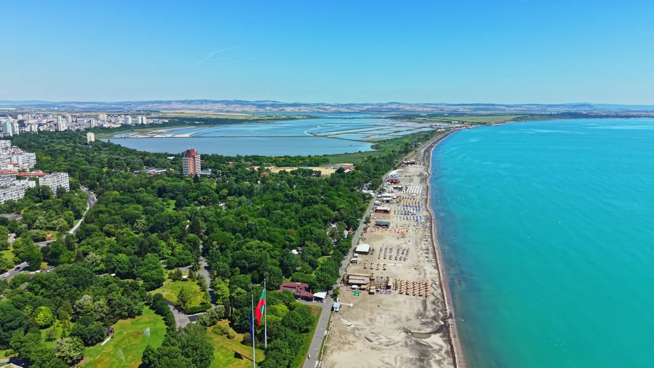 Gündüz saatlerinde güneşli bir konumda, mavi suları, kumlu sahili ve kıyı şeridindeki yeşil ağaçlarıyla bir plajın kıyı manzarası