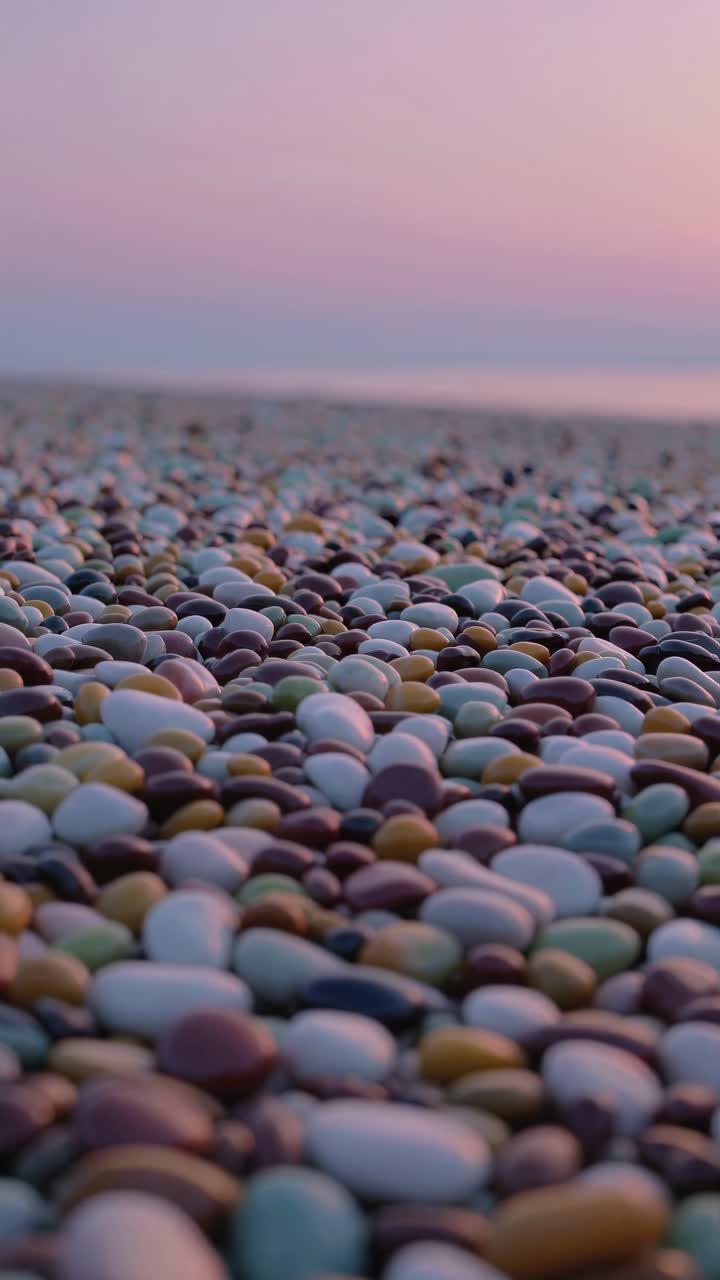 Close-up, low-angle video of colorful pebbles on a beach at sunset, capturing a serene and tranquil