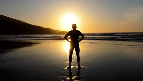silhouette of a man standing on beach at sunset, with golden sun and waves in background. orbiting shot