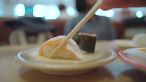 person picking up a piece of fresh salmon toro sushi with a pair of wooden chopstick in a sushi restaurant in numazu, shizuoka, japan