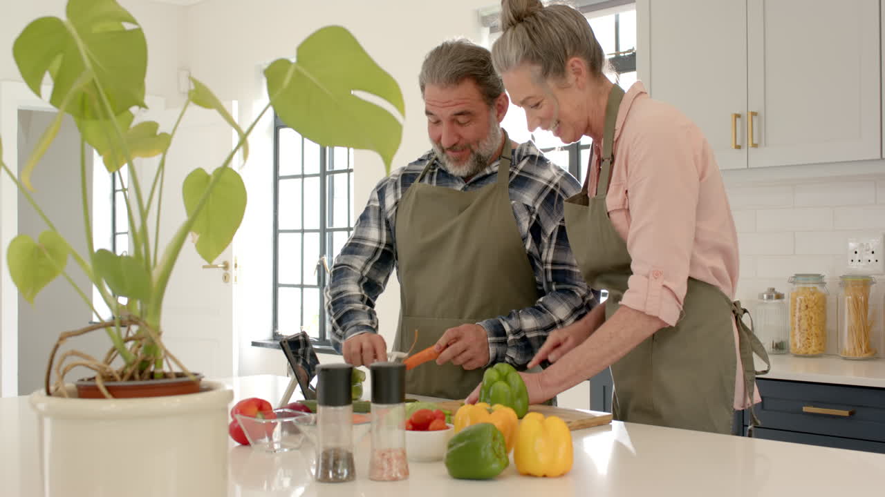 Coppia matura che prepara verdure insieme in cucina, divertendosi a cucinare a casa