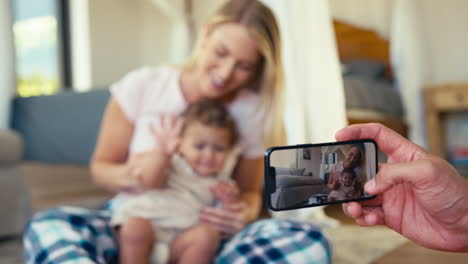 father recording video of mother and son sitting on sofa at home on  mobile phone