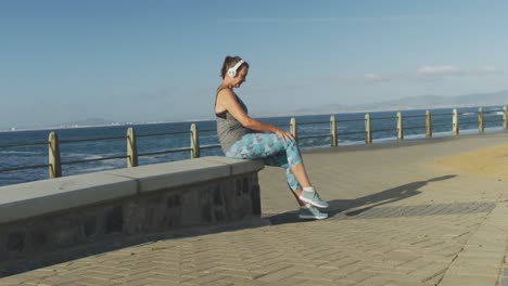 mujer mayor atando cordones de zapatos mientras corre en un paseo marítimo