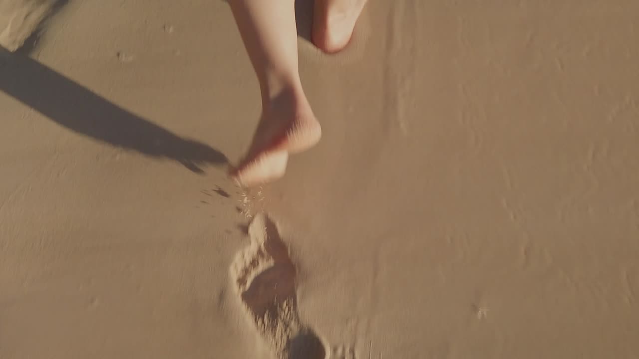 Primo piano dei piedi di una donna che camminano sulla sabbia della spiaggia, lasciando impronte e asciugando la sabbia