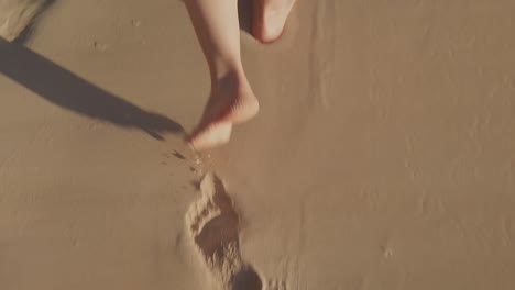 Un-Primer-Plano-De-Los-Pies-De-Una-Mujer-Caminando-Sobre-La-Arena-En-La-Playa,-Dejando-Huellas-Y-Secando-La-Arena