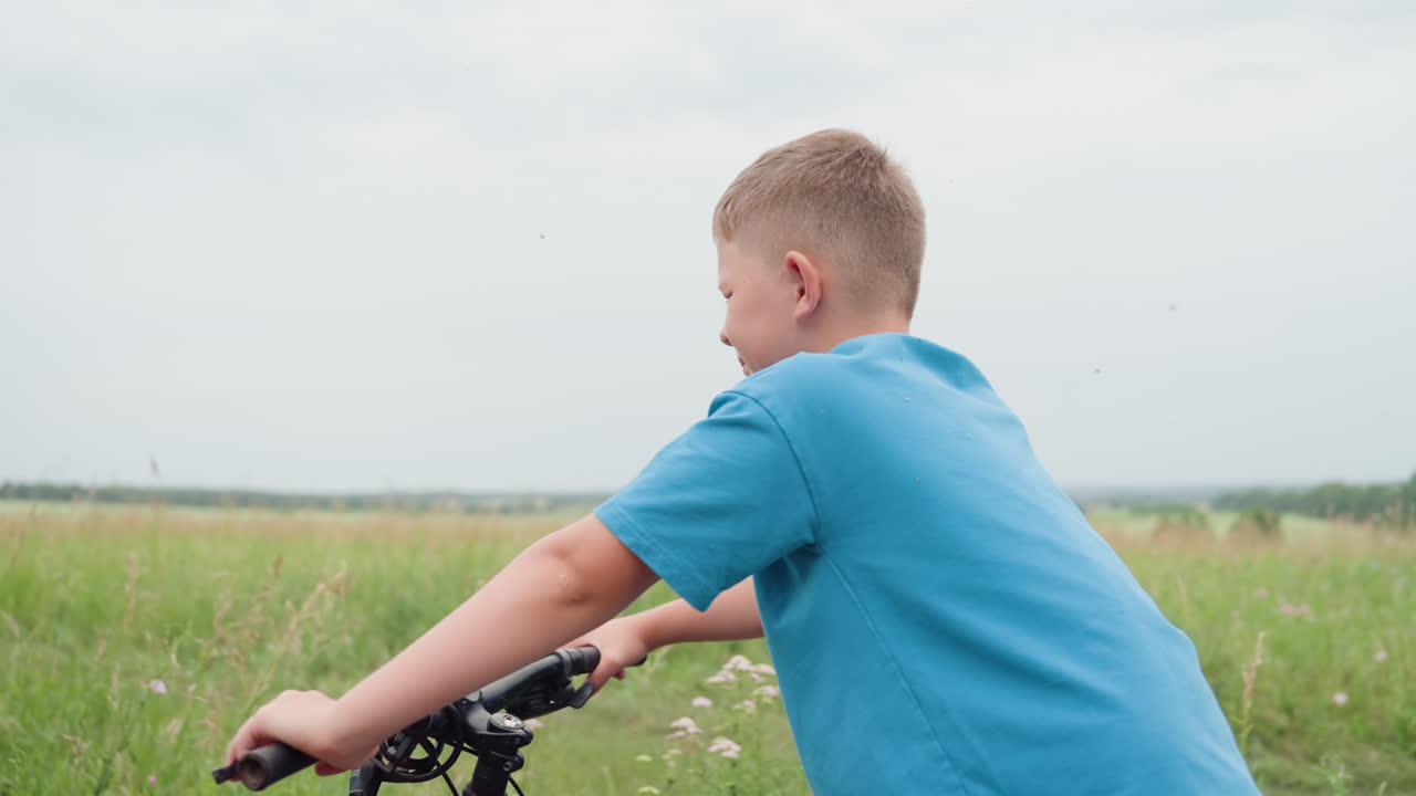 Caucasian boy riding bike through meadow on overcast summer day, hands on handlebar, pedaling across green field, glancing at horizon, relaxed smile, gentle breeze, countryside scenery evoking freedom