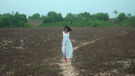 woman in white dress walking on dirt path through barren field, conveying a sense of solitude and reflection