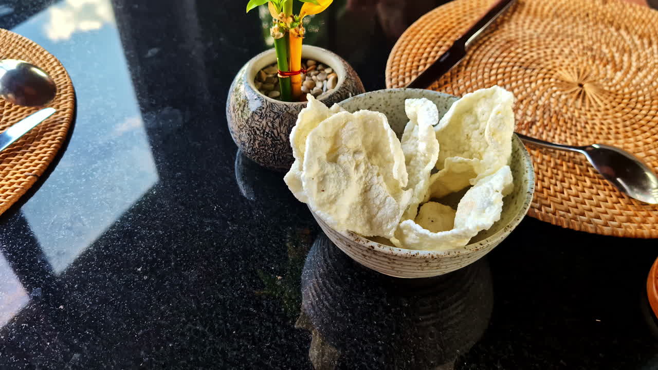 Hand reaching for crispy prawn crackers served in a ceramic bowl at a restaurant in Kuta Selatan, Bali, Indonesia