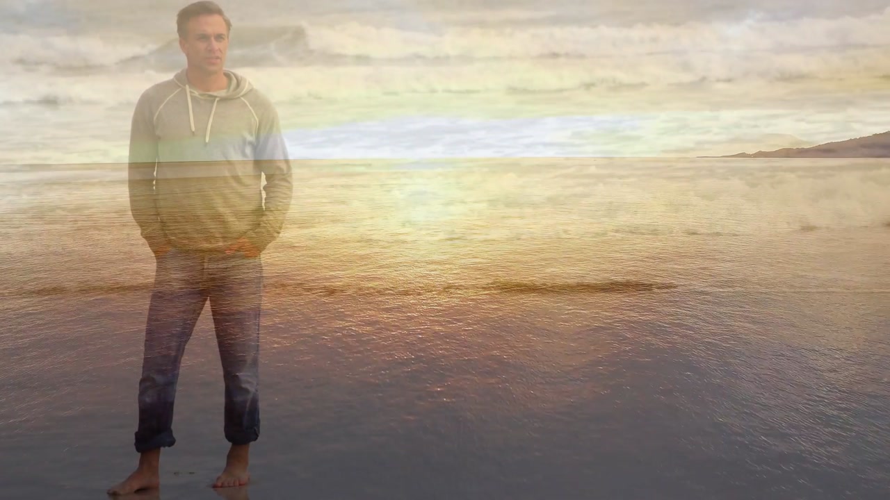 Man walking along reflective wet sand, leaving footprints, pausing while watching sunset for travel