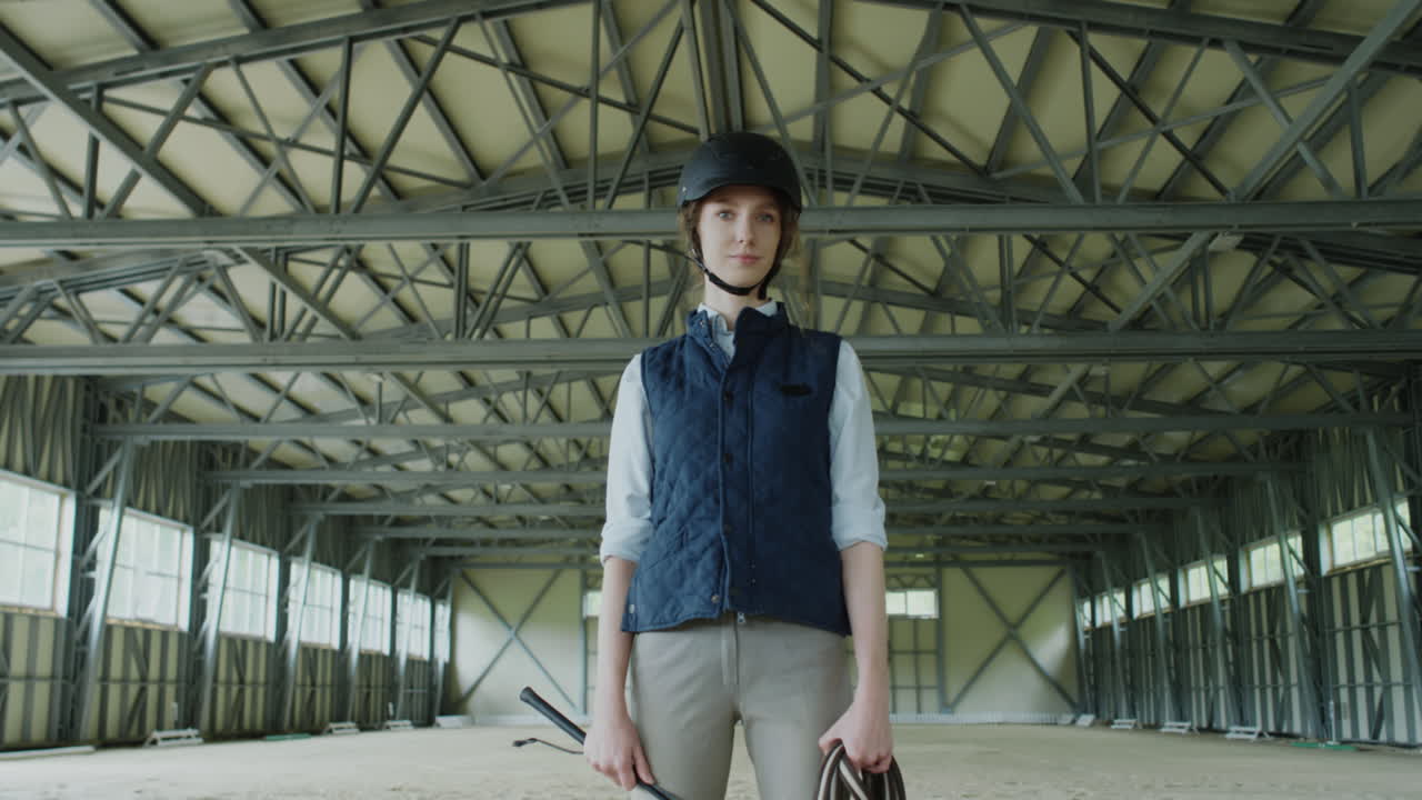 Woman in equestrian gear in an indoor riding arena with another rider
