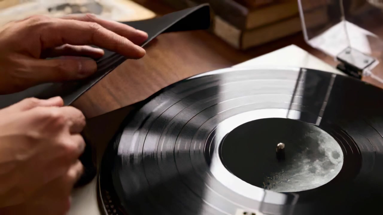 Sliding hands, right hand pulling sleeve off spinning vinyl on deck at home, revealing moon label