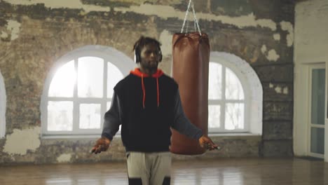 male boxer skipping the rope in and empty hall, listen music in headphones