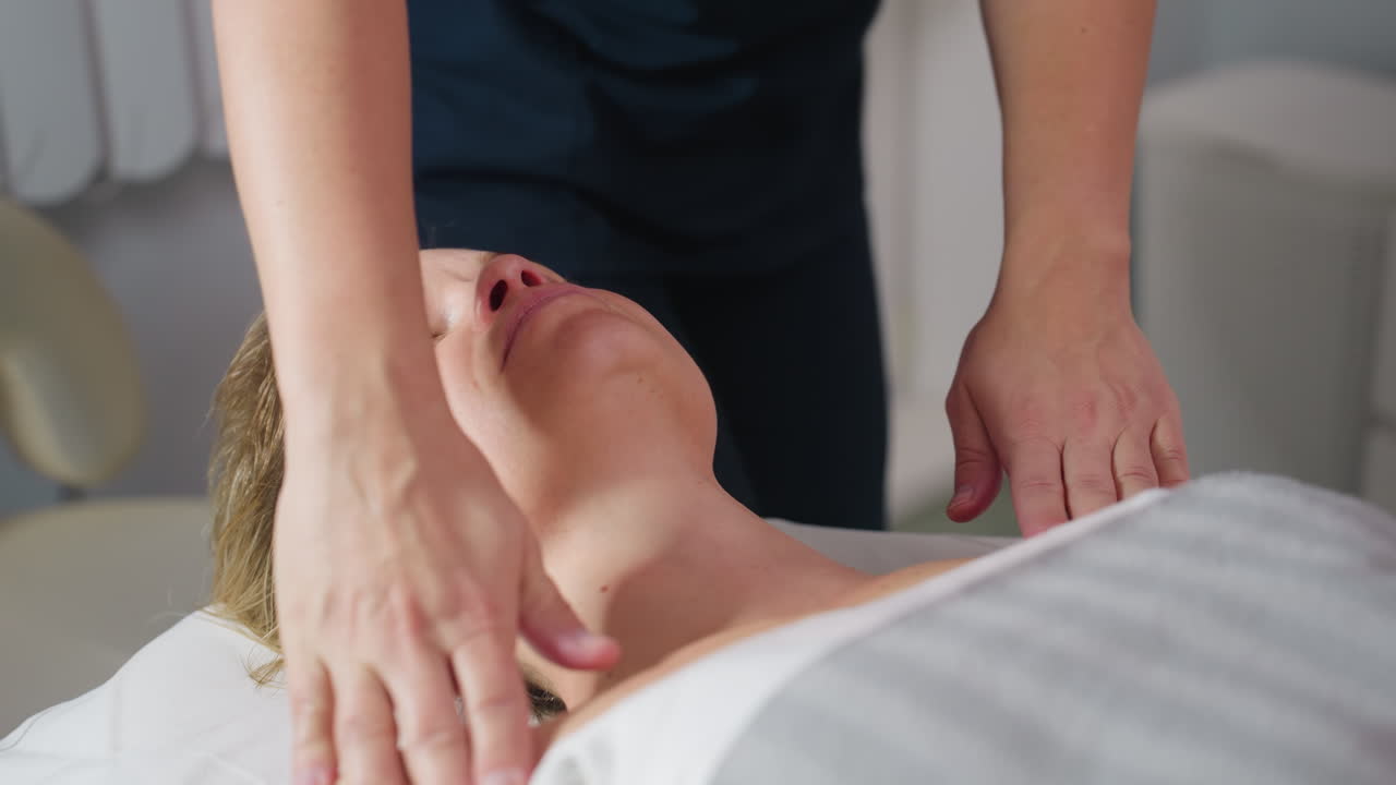 Wellness technician massaging neck of individual then rising to massage shoulders in serene spa room with soft lighting and skin care station visible adding sense of calm and gentle care