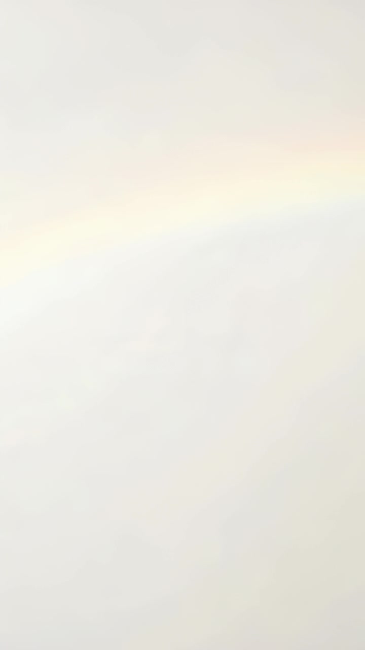 Vertical video: Streaming rainbow band crossing pale wall in room, coming from off-frame light