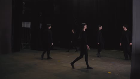 a group of confident young actors in black clothes enter the stage near a black curtain and at the same time stop practicing theatrical movement and freezing in place at a theater university