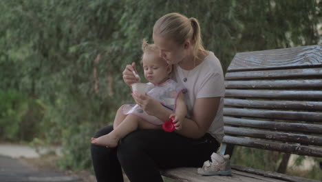 madre dando yogur a la hija bebé en el parque