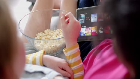 Diverse-teenage-female-friends-using-tablet-with-movies-and-eating-popcorn-at-home,-slow-motion