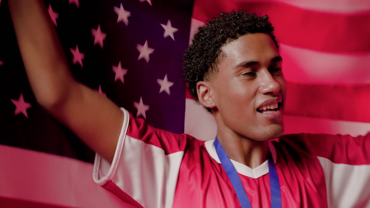 Uomo afroamericano che tiene la bandiera degli Stati Uniti sopra la testa, che indossa una maglia sportiva, con una medaglia blu, che festeggia una vittoria in studio.