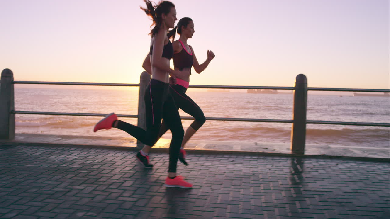 dos mujeres atléticas corriendo al aire libre en cámara lenta en el paseo marítimo al atardecer cerca del océano disfrutando de la carrera nocturna