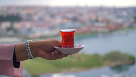 woman holding a glass of turkish tea with a city view