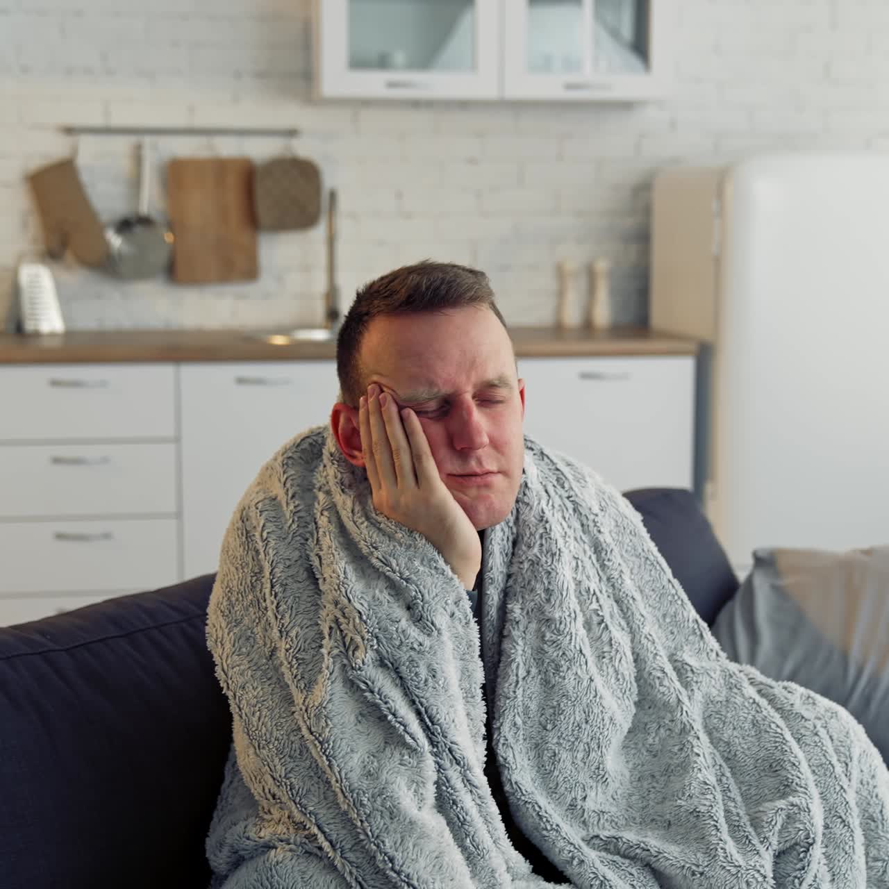 Unwell guy suffering coronavirus infection. Sick man with feeling ill and laying down on bed wrapped in blanket