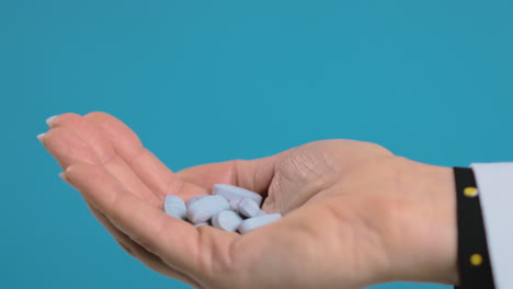 close up of pills falling into the hand of female doctor wearing white coat against blue background