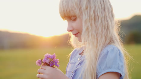 blonde girl 6 years old with a bouquet of wildflowers standing in the field at sunset side view slow