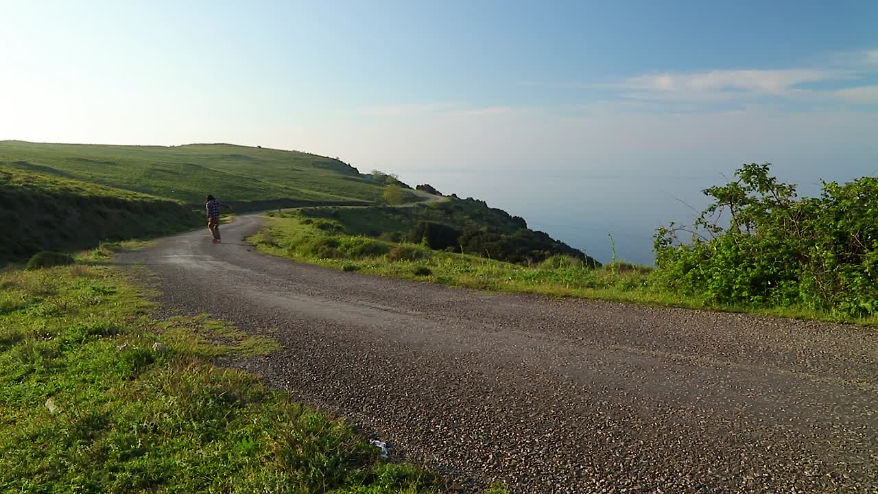 푸른 바다 옆에 있는 해변의 언덕을 통해 화려한 페니, 스케이트보드를 타고 내려가는 행복한 남자