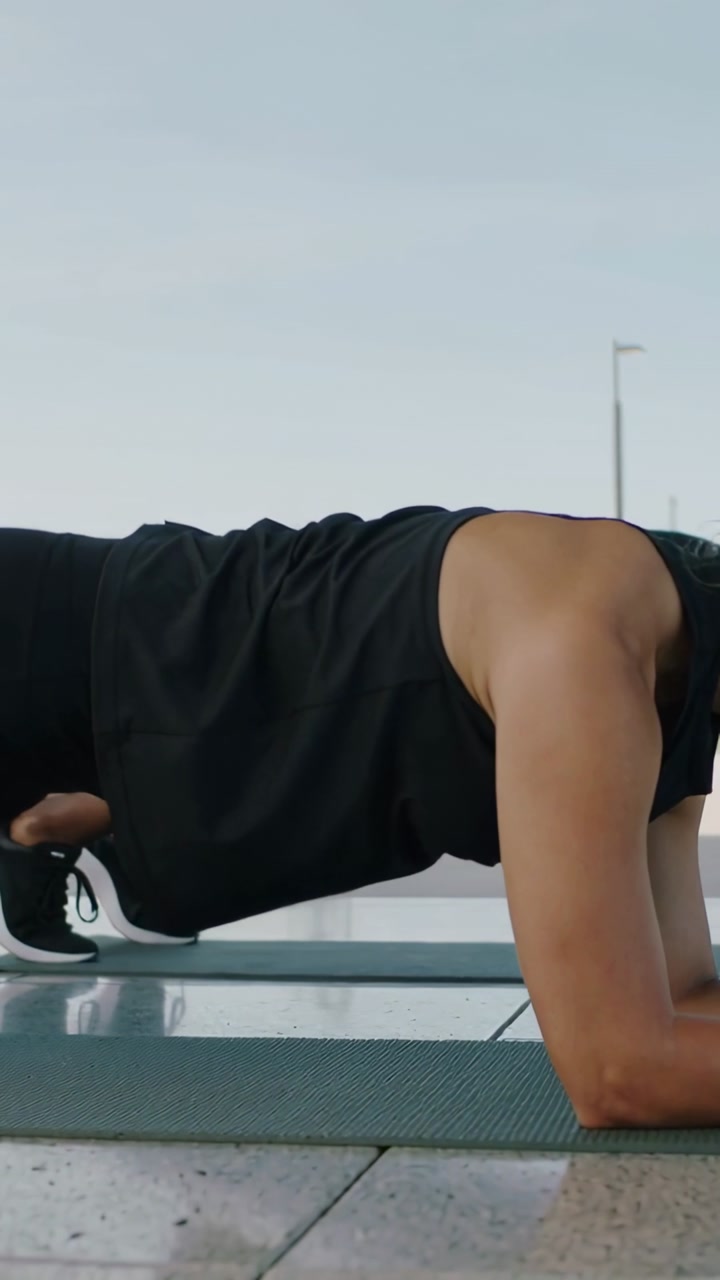 Female athlete holding forearm plank on yoga mat with feet on bench outdoors building core strength