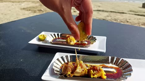 Hand-squeezing-calamansi-juice-over-pork-siomai,-a-traditional-Filipino-snack-while-enjoying-the-sunny-weather-at-the-beach