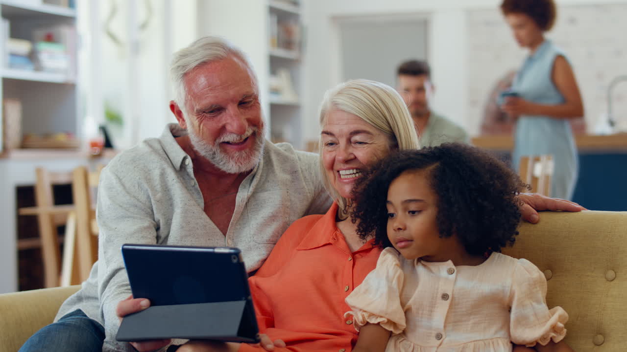Granddaughter And Grandparents On Sofa At Home Streaming Show On Digital Tablet