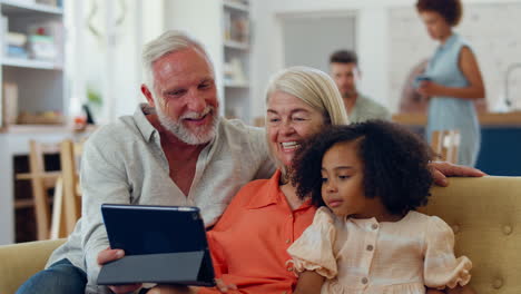 granddaughter and grandparents on sofa at home streaming show on digital tablet