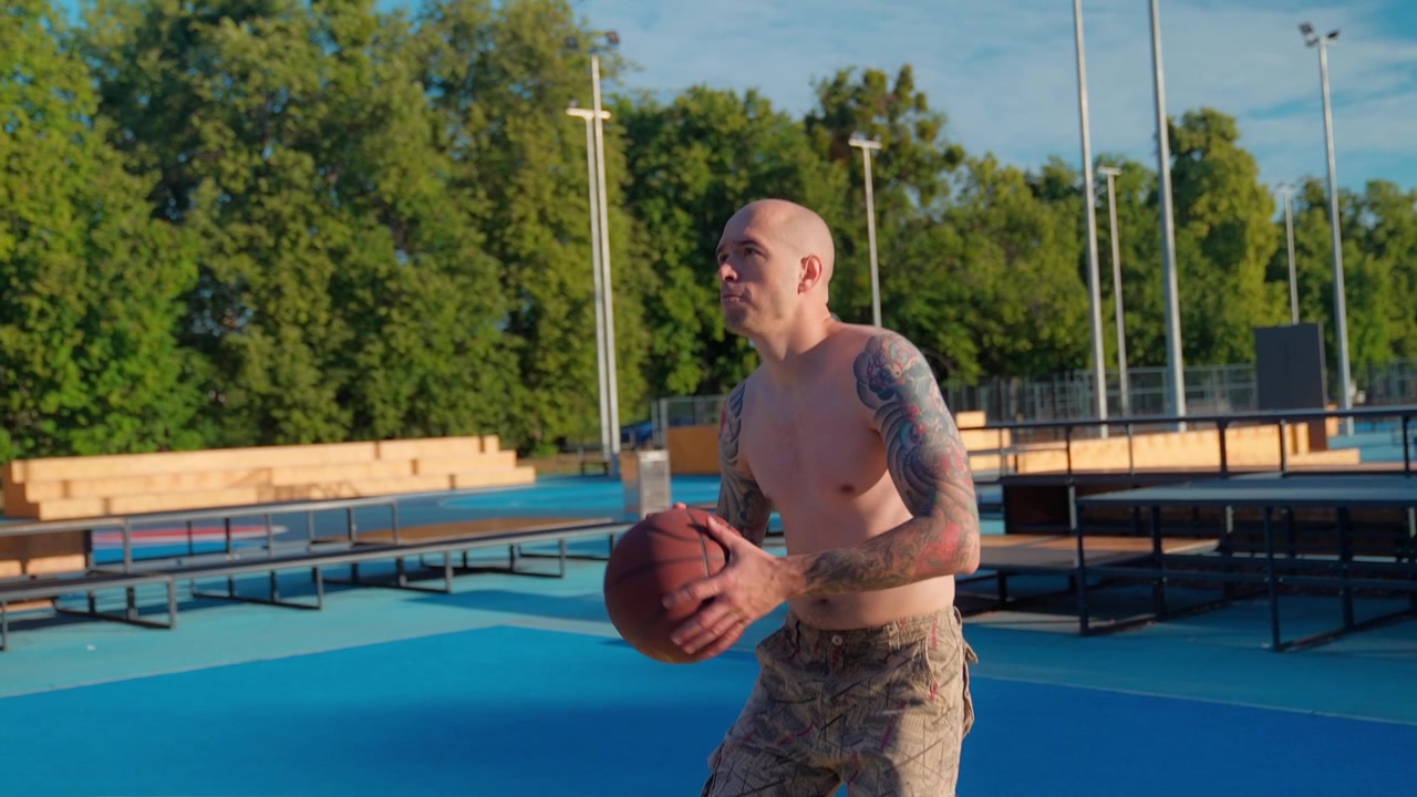 Uomo atletico a torso nudo si allena a tirare a canestro su un campo da basket all'aperto