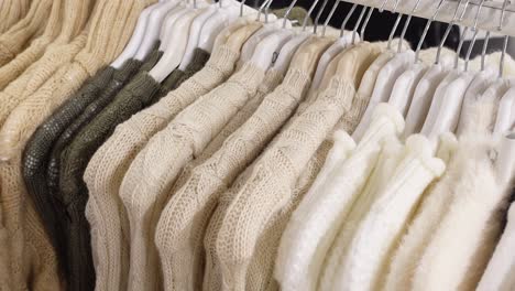 a rack of knitted sweaters in beige, white, and green