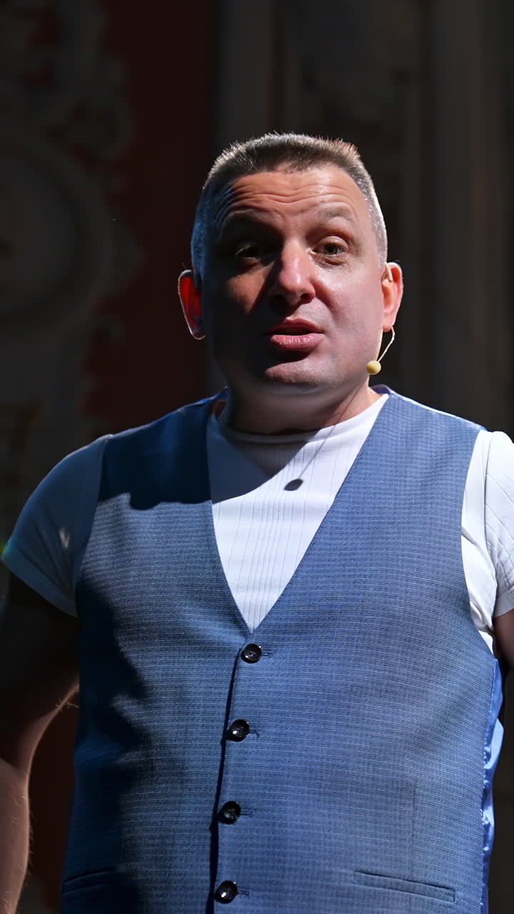 Man in suit speaking jokes in micropphone standing on stage. Funny performance. Comedian in good humor speaks to the audience. Vertical video