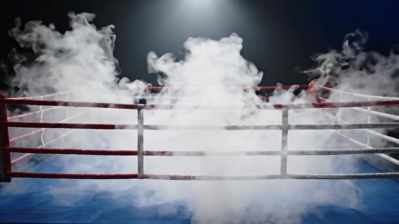 Un imponente ring di pugilato emerge dall'oscurità, illuminato da un riflettore e avvolto in una nebbia mistica durante uno scontro culminante.