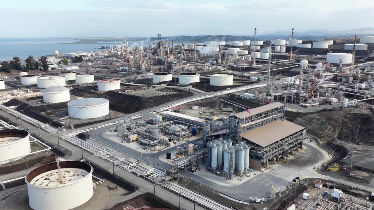 Extensive industrial landscape of Phillips 66 San Francisco Refinery in Rodeo, California, with white storage tanks and processing units along the coast. aerial drone orbit wide shot. Sunrise time.