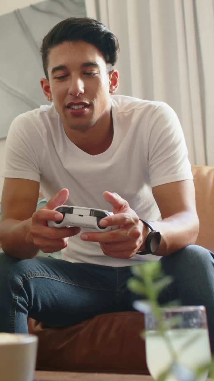 Vertical video: Playing man at game start with white controller on couch at home, grabbing drink