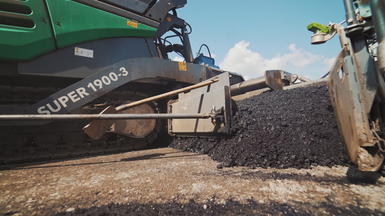 Construction and repair of highway. Pavement machine laying fresh asphalt on top of the gravel base during highway construction