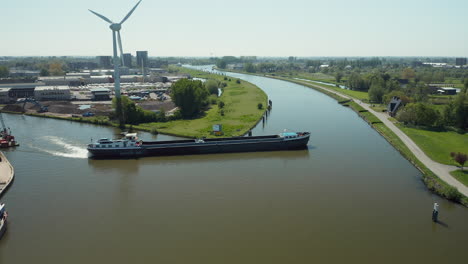 a flat-bottomed boat cruising the tranquil waters of gouwe river with wind turbine on sight and panoramic environment of zuidelijk halfrond province, in south holland, netherlands